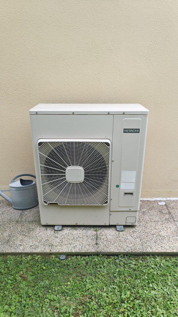Groupe extérieur de climatisation posé sur socle dans un jardin