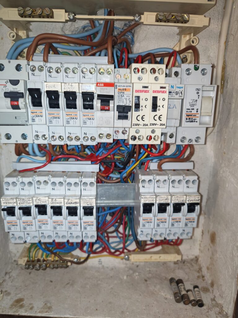 Tableau électrique ouvert, disjoncteurs et câblage en cours de reprise