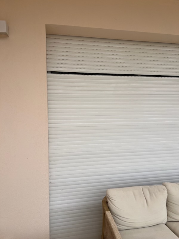 Volet roulant blanc fermé sur une baie, vu de l'intérieur