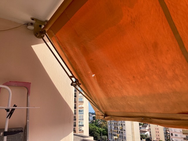 Store banne à toile orange déployé au-dessus d'une terrasse, vu de dessous